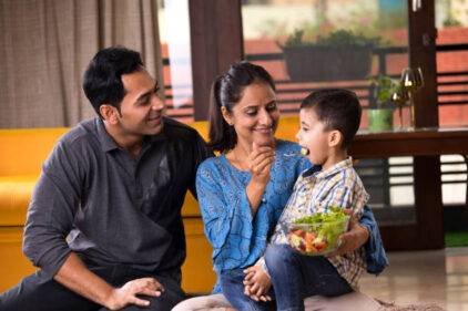 Happy family with woman feeding fruit salad to her son